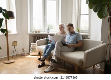 Serious Older Couple Sit On Couch At Home With Laptop Learn Legal Documents, Sorting Out Papers, Making Online Payment, Discuss Expenses, Reviewing Utility Bills, Control Manage Family Budget Concept