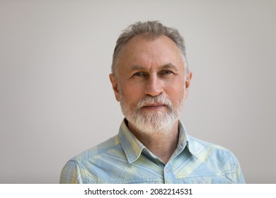 Serious older man in casual with beard head shot portrait. Grey haired retiree, pensioner posing, standing isolated against white wall background. Close up male portrait, elderly age concept