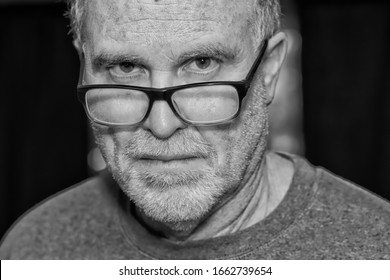 Serious Older Man Stares With His Glasses On His Nose In Black And White