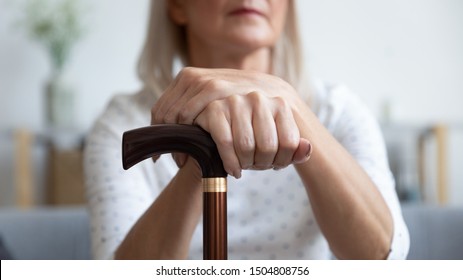 Serious Older Woman Holding Hands On Wooden Cane Close Up, Sitting And Resting On Couch At Home, Disabled Older Female Using Walking Stick During Rehabilitation, Older People Healthcare