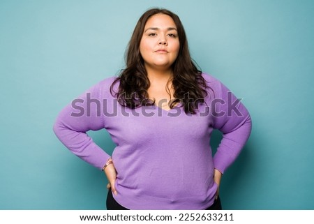 Serious overweight hispanic woman with her hands on the hips looking determined while making eye contact