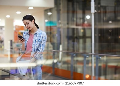 Serious Pensive Attractive Girl In Casual Clothing Standing In Corridor And Using Messenger On Phone While Wasting Time In Airport Terminal