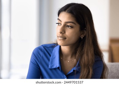 Serious pensive beautiful Indian woman looking away with focus on deep thoughts, sitting on home couch, thinking on problems, troubles. Thoughtful silent young adult girl making decision - Powered by Shutterstock