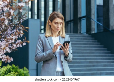 Serious And Pensive Business Woman Uses The Phone Outside The Office, Looking At The Smartphone Screen