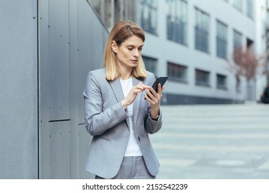 Serious And Pensive Business Woman Uses The Phone Outside The Office, Looking At The Smartphone Screen