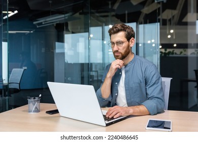 .Serious pensive businessman in shirt thinking about decision sitting at table in modern office, man with beard is using laptop at work. - Powered by Shutterstock