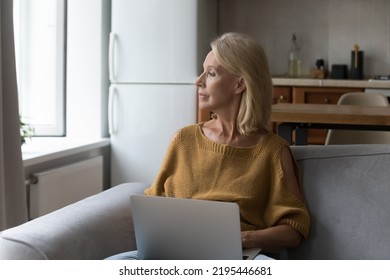 Serious Pensive, Deep Of Thoughts Older Woman Spend Time At Home, Thinking, Resting With Laptop Seated On Sofa, Staring Out Window Looking Thoughtful, Consider Purchase, Distracted From Computer