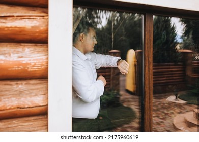 A Serious, Pensive Man, A Businessman In A White Shirt Stands Near The Window In Anticipation, Looking At The Wristwatch On His Hand. Portrait, Photography.