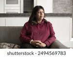 Serious pensive mature Indian woman looking away with thoughtful face from home couch, sitting on sofa, daydreaming, thinking on troubles, problem solving, making decision