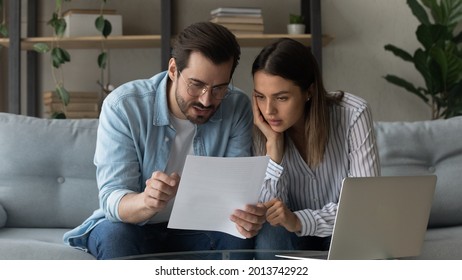 Serious pensive millennial 35s couple sit on sofa at home hold letter reading papers documents, learn details of contract, discuss agreement terms conditions, considering mortgage loan offer concept - Powered by Shutterstock