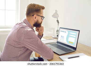 Serious Pensive User Visiting Landing Page Website Of Online Service Or Company. Man Sitting At Desk In Home Office And Thinking What Personal Information And Email Query To Write In Contact Us Form