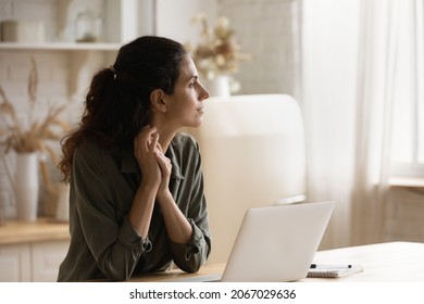Serious pensive woman sit in kitchen at table with opened laptop looks into distance thinking, ponder, distracted from telecommuting, search for solution, daydream alone at home. Modern tech concept