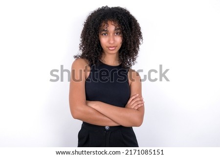 Serious pensive Young beautiful girl with afro hairstyle wearing black t-shirt over white background feel like cool confident entrepreneur cross hands.
