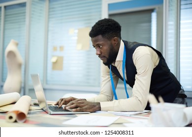 Serious pensive young black tailor with beard working in own studio: he making online pattern on laptop - Powered by Shutterstock