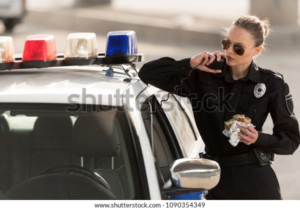 serious policewoman with burger in hand talking on radio\
set 