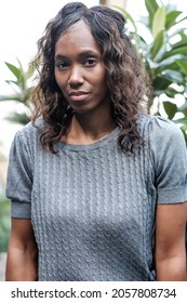 Serious Portrait Of Mature Black Woman Looking To Camera. Plants Behind Her.