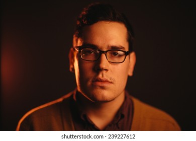 Serious Portrait Of A Young Adult Man With Glasses Staring At Camera Orange Lighting