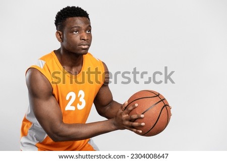 Serious, professional african basketball player holding basketball, looking concentrated isolated on white background. Young sportsman wearing orange uniform, performing exercises