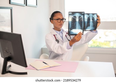 Serious pulmonologist comparing two x-ray pictures of lungs. Young African American doctor sitting at table examining x-ray radiography in her office. Radiology research, pneumonia or asthma concept - Powered by Shutterstock