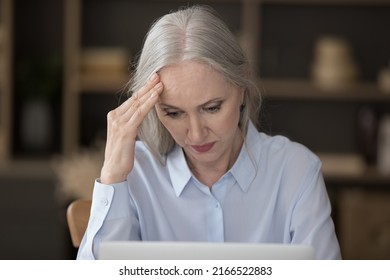 Serious puzzled older businesswoman sit at desk looks at laptop touch head feels stressed due to info overload, faced with difficult task, lack of understanding of tech, new software, bad news concept