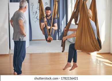 Serious Qualified Young Caucasian Coach Sitting In A Silk Hammock During The Aerial Yoga Class