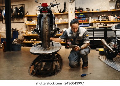 Serious repairman with tablet computer examining motorcycle - Powered by Shutterstock