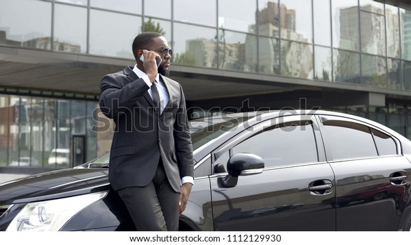 Serious rich man in expensive business suit talking\
over phone in big city