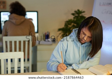 Serious school student reading thick book and taking notes in textbook