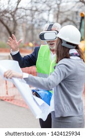 Serious Senior Architect Or Businessman Using Virtual Reality Goggles To Visualize Construction Project On A Construction Site. Young Female Engineer Holding Blueprints