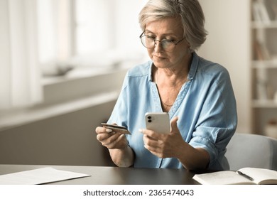 Serious senior bank client woman paying on Internet by credit card, using financial app on mobile phone for online transactions, payment, sitting at workplace table - Powered by Shutterstock