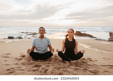 Serious senior caucasian lady and man in sportswear practice yoga and breathing exercises with closed eyes on beach in morning, outdoor. Meditation together, rest, relax and peace - Powered by Shutterstock