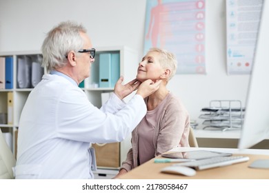 Serious Senior Male Oncologist With Gray Hair Sitting In Front Of Mature Female Patient And Touching Her Neck During Checkups