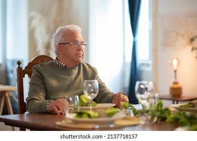 Serious Senior Man Wearing Glasses Sitting At Party Table. Portrait Of Elder Man Having Dinner Alone At Home. Elderly People Concept