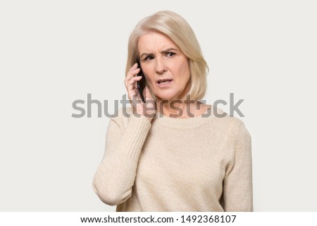 Serious senior mature woman isolated on grey studio background hold cellphone talking discussing problems, focused aged lady using smartphone, speak with wireless 5g connection, technology concept
