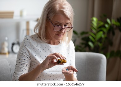 Serious senior woman in glasses sit on couch having daily vitamins or diet supplements at home, mature old female pensioner take dose of pills from meds bottle, elderly healthcare, medication concept - Powered by Shutterstock