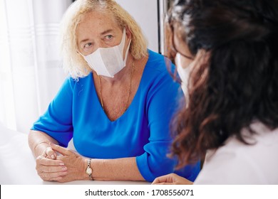 Serious Senior Woman In Medical Mask Listening To Doctor Visiting Her At Home And Talking About Danger Of The Virus