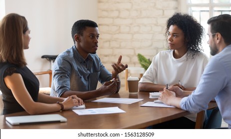 Serious skilled african american young manager explaining market research results to concentrated mixed race teammates. Focused diverse employees listening to biracial colleague at meeting in office.