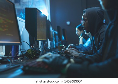 Serious smart coders sitting in line in dark server room and using modern computers while working on apps