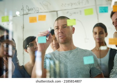 Serious, smart and creative design team brainstorming a strategy idea and writing on sticky notes on a transparent board. Group planning and working in close collaboration together in a meeting - Powered by Shutterstock