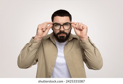 Serious smart millennial middle eastern man adjusting glasses, focused gaze, with thoughtful expression, isolated on gray background. News, bad vision problems, myopia and emotions - Powered by Shutterstock