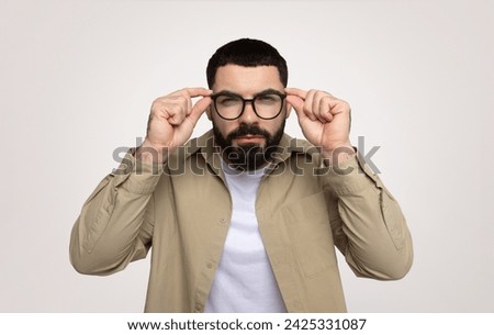 Serious smart millennial middle eastern man adjusting glasses, focused gaze, with thoughtful expression, isolated on gray background. News, bad vision problems, myopia and emotions