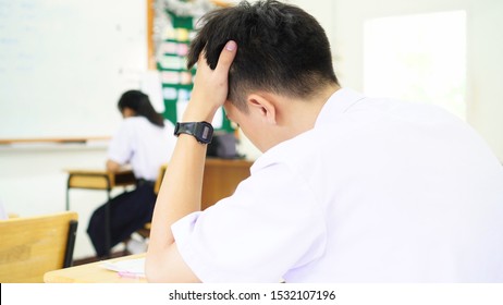 Serious Stressed Headaches, Asian Boy Student Studying For Test Or Exams In Classroom, Learning Lessons Doing Final Exam At High School With Thailand Uniform In Class Room. Education System Concept.