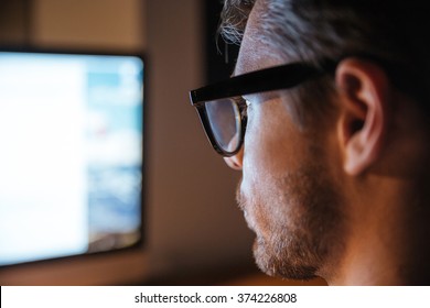 Serious stubbled young man in glasses using computer and looking at screen