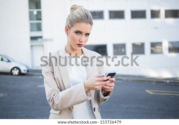 Serious stylish businesswoman sending a text\
outdoors on urban\
background