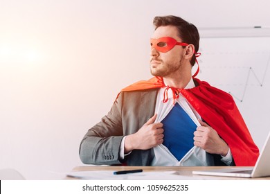 serious super businessman in mask and cape showing blue shirt in office - Powered by Shutterstock