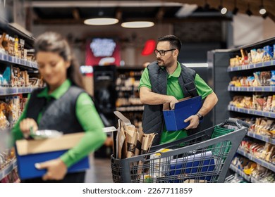 A serious supermarket worker is arranging and putting groceries on aisle at market. - Powered by Shutterstock