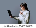 Serious surprised middle aged woman using laptop on grey background