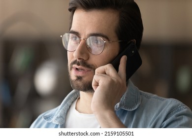 Serious talk. Concentrated young casual businessman in glasses hold smartphone to ear make answer business call contact client. Confident male expert consult customer by phone on professional matter