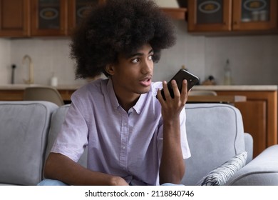 Serious Teen African Hipster Guy Recording Audio Message On Mobile Phone, Using Voice Recognition App, Making Cellphone Call, Talking To Virtual Assistant Service, Sitting On Home Sofa