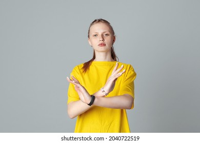 Serious teen girl making X sign with her arms to stop doing something, isolated on light grey background, wearing in casual blank yellow t shirt. Stop, no, stay back. Concept of warning, prohibition